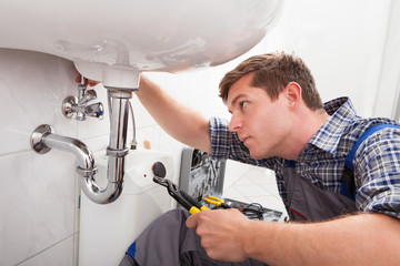 The Plumbing Services technician repairing leaking drain pipes under sink